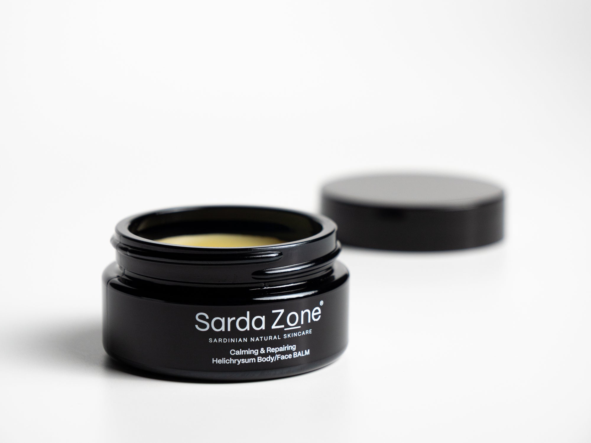 Open jar of Sarda Zone Helichrysum Body/Face BALM on a white background with the lid behind it